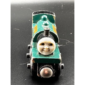 May include: A green wooden toy train featuring a smiling face and the name "Stanley" on the side. The train has black wheels and a black smokestack. The paint shows signs of wear.