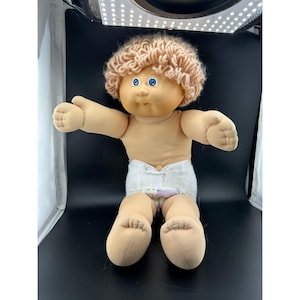 May include: A vintage Cabbage Patch Kid doll with a tan complexion, blue eyes, and light brown curly hair. The doll is wearing a diaper and is posed with arms outstretched.
