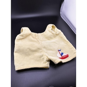 Pode incluir: Calções de bebé em veludo cotelê amarelo claro com alças. Os calções apresentam um design de barco bordado com detalhes em vermelho, branco e azul. A peça de vestuário é feita de tecido de veludo cotelê canelado.