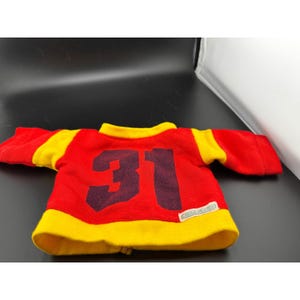 Könnte beinhalten: Ein rot-gelbes Trikot mit der Nummer 31 in Dunkelviolett. Das Trikot hat gelbe Ärmel und einen gelben Kragen. Das Trikot hat unten ein kleines Etikett mit der Aufschrift "CARLTON".