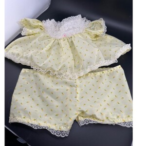 May include: A two-piece set consisting of a pale yellow short-sleeved top and matching shorts. The top features a white lace collar and trim, while both pieces are decorated with a small yellow floral print and finished with white lace edges.