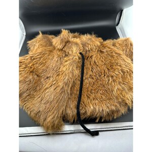 May include: A brown faux fur garment with a black drawstring. The fur is a warm, medium brown color. The garment appears to be a vest or a similar type of outerwear. The black drawstring is visible in the center.