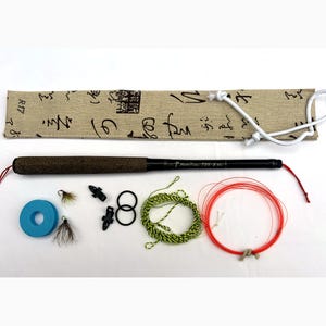 Puede incluir: Una caña de pescar tenkara con mango de corcho, una funda de tela beige con caligrafía negra, dos moscas con plumas, un devanador de espuma azul, dos clips de plástico negro, dos juntas tóricas negras, un sedal amarillo y negro y uno rojo.