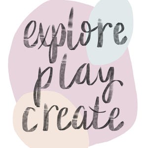May include: A digital art print with the words "explore play create" in a handwritten style. The text is in dark gray against a light pink background with pastel-colored shapes.