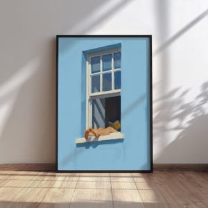 Puede incluir: Una impresión artística enmarcada representa una pared exterior azul con una ventana blanca. La ventana está abierta y una persona descansa en el alféizar, leyendo un libro. La obra de arte se exhibe sobre un suelo de madera.