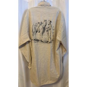 Op de afbeelding: Beige button-down shirt met een zwart-wit illustratie van een persoon en een paard op de rug. Het shirt met lange mouwen heeft een kraag en een relaxte pasvorm.