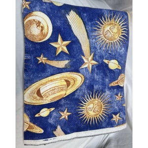 May include: A rectangular fabric piece featuring a deep blue background with a celestial pattern. The design includes golden yellow illustrations of suns with faces, various planets with rings, multiple stars, and shooting comets scattered throughout.