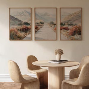 May include: Three framed landscape art prints with text. The prints feature a road winding through a mountain scene with text that reads "ASK", "SEEK", and "KNOCK". A round wooden table and chairs are in the foreground.