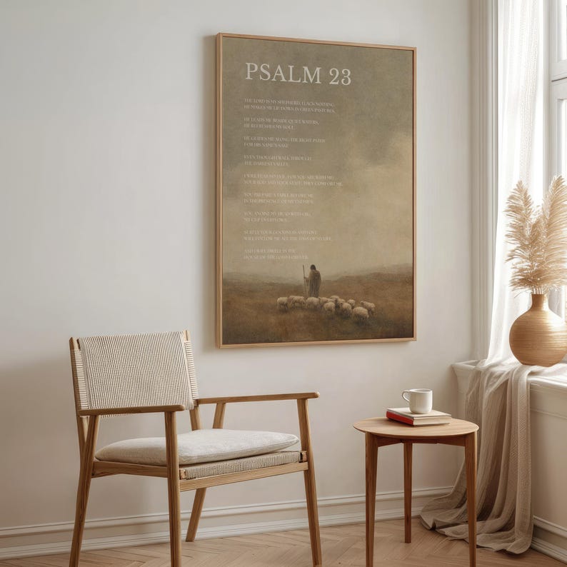 May include: A framed print with the text "PSALM 23" at the top. The artwork depicts a shepherd with sheep in a field, with a muted color palette. A wooden chair and small table with a mug and books are in the foreground.