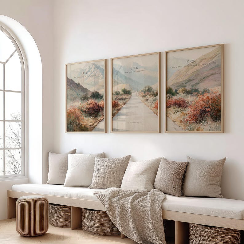 May include: Three framed landscape art prints with the words "Ask", "Seek", and "Knock" in a light beige frame. The prints depict a road winding through a mountain landscape with muted colors. The room also features a bench with pillows and a woven basket.