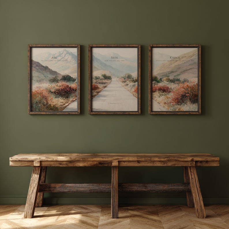 May include: Three framed landscape prints with the words "Ask", "Seek", and "Knock" above a road leading into the distance. The prints are in wooden frames and hang on a dark green wall above a rustic wooden bench.