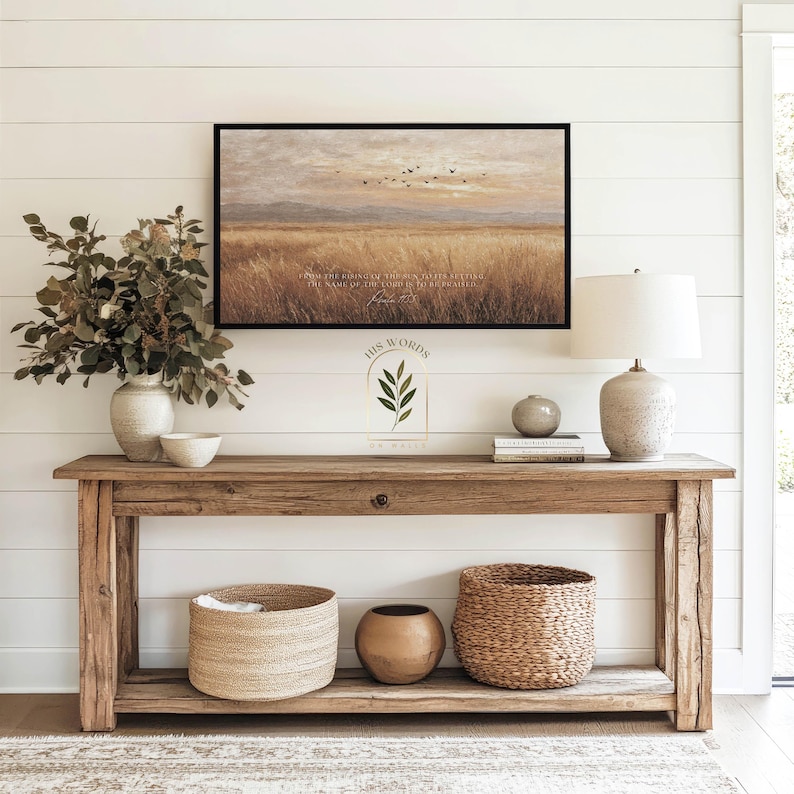 May include: A rustic wooden console table with a framed landscape painting, a lamp, and decorative baskets. The painting depicts a field with birds in flight. The text "HIS WORDS" is visible on the wall.