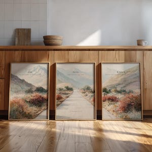 May include: Three framed landscape art prints with inspirational text. Each print features a watercolor painting of a path leading through a mountain valley. The text on the prints reads "Ask", "Seek", and "Knock". The frames are a light brown color.