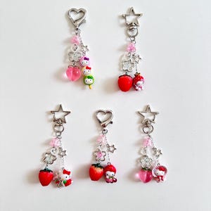 Peut inclure: Cinq porte-clés avec différents breloques. Chaque porte-clés a un charme en forme de cœur ou d'étoile argenté avec une chaîne attachée. Les breloques comprennent une pêche rose, une fraise, un dango vert et un personnage Hello Kitty.