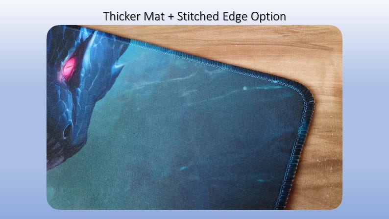 May include: A rectangular desk mat featuring a dark blue and teal dragon graphic with a glowing red eye. The mat has a stitched edge and the text Thicker Mat + Stitched Edge Option is displayed above the product in the image frame.