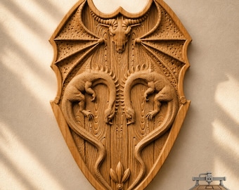 May include: A shield-shaped wooden wall plaque featuring a carved relief of a horned skull at the top, flanked by two symmetrical dragon figures with textured wings. The wood grain is visible throughout the piece, and the text CNC ROUTER IDEAS is printed in the bottom right corner.