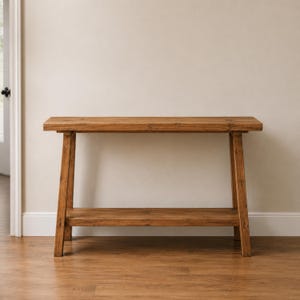 May include: A rectangular wooden console table with a natural brown finish, featuring a flat top surface and a lower shelf supported by four angled legs. The table is constructed from wood with a visible grain pattern and a smooth, matte texture.