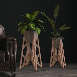 May include: Two wooden plant stands with geometric designs hold potted plants with green foliage. The stands are light brown and have a modern aesthetic. A dark brown leather armchair is on the left side of the image.