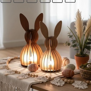 Könnte beinhalten: Zwei holzgeschnitzte Hasenlampen mit leuchtenden Innenräumen stehen auf einem Holztisch. Die Lampen befinden sich neben dekorativen Ostereiern und einem Weidenkorb. Der Tisch hat auch einen dekorativen Tischläufer und eine Kette aus Holzperlen. Der Text "DIGITAL FILE" steht oben.