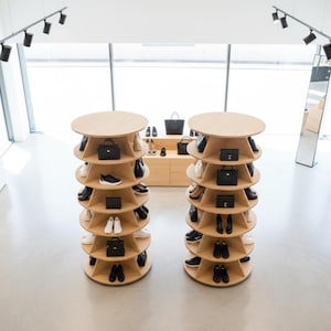 K&ouml;nnte beinhalten: Moderne Ladenauslage mit zwei kreisf&ouml;rmigen Holzregalen, die Schuhe und Handtaschen pr&auml;sentieren. Die Regale sind spiralf&ouml;rmig angeordnet, wobei jede Ebene verschiedene Stile zeigt. Der Laden hat ein minimalistisches Design mit heller Beleuchtung.