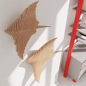 May include: Two wooden wall sculptures in the shape of stingrays, with a layered, 3D design. The sculptures are mounted on a white wall, with a red ladder shelf in the background.