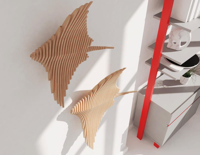 May include: Two wooden wall sculptures in the shape of stingrays, with a layered, 3D design. The sculptures are mounted on a white wall, with a red ladder shelf in the background.