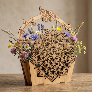 Könnte beinhalten: Ein Blumenkorb aus Holz mit einem lasergeschnittenen Mandala-Design. Der Korb ist mit einer Vielzahl bunter Wildblumen gefüllt, darunter Gänseblümchen, Kornblumen und Klee. Der Griff ist mit floralen Ausschnitten verziert.