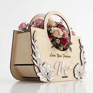 May include: A wooden flower basket with a handle, filled with pink and red roses. The basket is decorated with floral cutouts and the words "Love You Forever Mom".