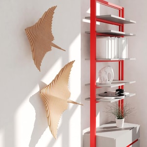 May include: Two wooden wall sculptures in the shape of stingrays, mounted on a white wall. A red metal shelf unit with gray shelves is on the right side of the image.
