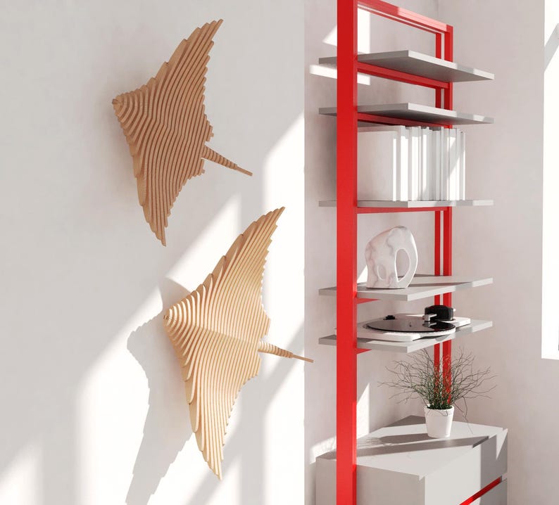 May include: Two wooden wall sculptures in the shape of stingrays, mounted on a white wall. A red metal shelf unit with gray shelves is on the right side of the image.