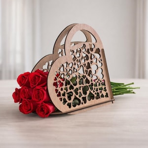May include: A wooden heart-shaped flower basket with a handle, filled with vibrant red roses. The basket has a decorative cutout design of hearts. The roses are fresh and the stems are visible.
