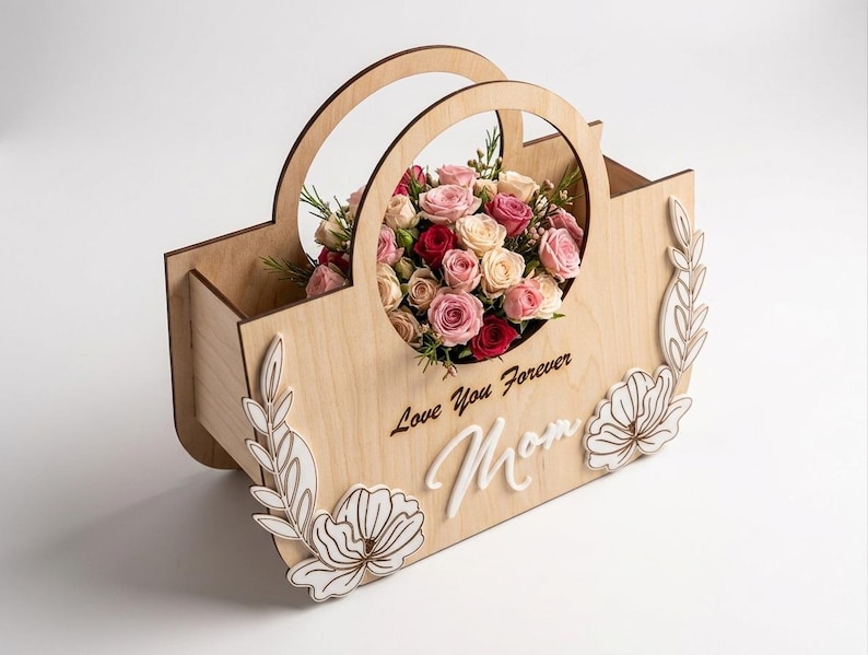 May include: A wooden flower basket with a handle, filled with pink, red, and cream-colored roses. The basket has decorative floral cutouts and the words "Love You Forever Mom" engraved on the front.