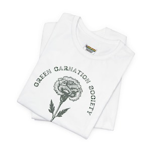 May include: A white short-sleeved t-shirt featuring a dark green graphic of a single carnation flower centred on the chest. The text "GREEN CARNATION SOCIETY" is printed in a dark green arched font around the flower illustration.