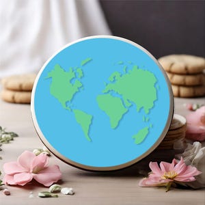 May include: A round, light blue and green Earth-shaped decorative item. The continents are green, set against a blue background. The item is surrounded by a white and brown border. Pink flowers and cookies are in the background.