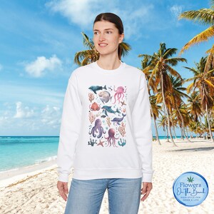 May include: White sweatshirt featuring a colourful print of various sea creatures, including octopuses, fish, and starfish. The print is in a watercolour style and features shades of blue, pink, and purple.