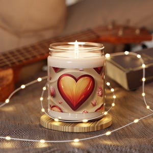 Peut inclure: Une bougie allumée dans un bocal en verre avec un motif de cœur. La bougie repose sur un dessous de verre en bois, entourée de guirlandes lumineuses. Le cœur est rouge et jaune, avec des coquillages. C'est une bougie de soja.