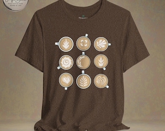 Puede incluir: Camiseta marrón con un diseño de nueve tazas de café con diferentes diseños de arte latte. El diseño está centrado en la camiseta.