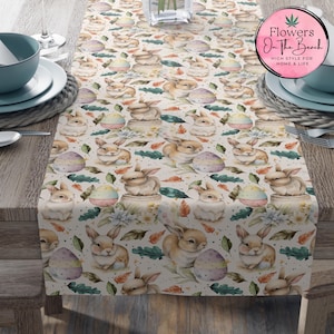 May include: A white table runner with a repeating pattern of watercolor bunnies holding Easter eggs, green leaves, and white flowers. The table runner is decorated with a light brown background and small white dots.