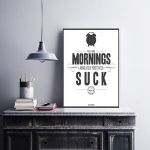 May include: Black and white typography poster with the text "Rise & Shine Mornings Absolutely Positively Suck" and a clock icon. The poster is framed and hanging on a wall.