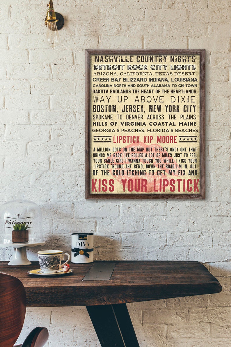 K&ouml;nnte beinhalten: Ein Vintage-Poster mit einem rustikalen Holzrahmen, das einen Songtext aus "Lipstick" von Kip Moore zeigt. Das Poster hat einen wei&szlig;en Hintergrund mit rotem und schwarzem Text. Der Text lautet: "Nashville Country Nights, Detroit Rock City Lights, Arizona, California, Texas Desert, Green Bay Blizzard Indiana, Louisiana, Carolina North and South Alabama to Chi Town, Dakota Badlands the Heart of the Heartlands, Way Up Above Dixie, Boston, Jersey, New York City, Spokane to Denver Across the Plains, Hills of Virginia Coastal Maine, Georgia's Peaches, Florida's Beaches, ***** Lipstick Kip Moore *****, A million dots on the map but there's only one that brings me back I've rolled a lot of miles just to feel your smile girl I wanna touch you while I kiss your lipstick 'round the bend, down the road I'm in. Out of the cold itching to get my fix and Kiss Your Lipstick."