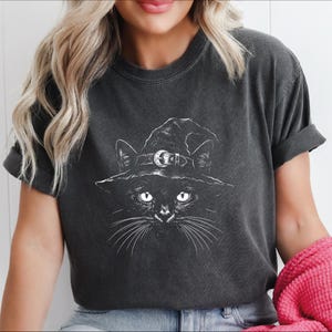 Close-up of a charcoal garment-dyed tee, white etched black cat in a witch hat with whiskers spreading across the chest.