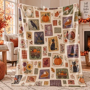May include: A cream-colored throw blanket featuring a patchwork-style print of autumn and Halloween motifs, including pumpkins, black cats, a skeleton, a ghost, a witch hat, a turkey, slices of pie, sunflowers, and various fall leaves.