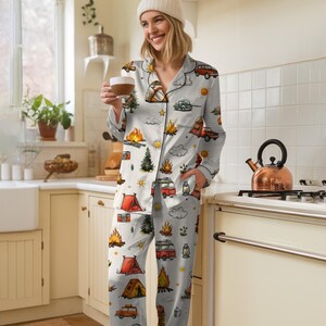 以下が含まれることがあります： キャンプをテーマにしたライトグレーのパジャマセット。ボタンダウンシャツとパンツのセットで、テント、キャンプファイヤー、木、ヴィンテージキャンピングカーのイラストが描かれています。パジャマは柔らかい素材で作られています。