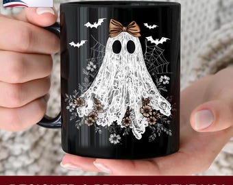 May include: Black ceramic mug featuring a white ghost design with a brown bow, bats, and spiderwebs. The ghost is adorned with a lace-like pattern and floral accents. The mug has the text "PRINTED ON BOTH SIDES" and "DESIGNED & PRINTED IN THE USA".