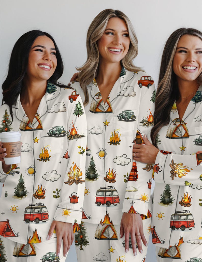 以下が含まれることがあります： クリーム色のパジャマセット。キャンプをテーマにしたパターンで、キャンプファイヤー、テント、ヴィンテージカー、木、赤いキャンピングカーのイラストが含まれています。パジャマはボタンダウンシャツとマッチングパンツです。