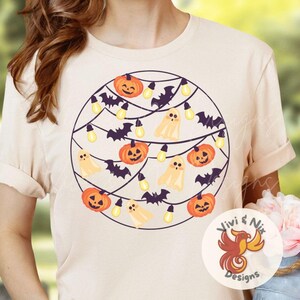 May include: Cream-colored t-shirt featuring a circular design with Halloween-themed illustrations. The design includes orange jack-o'-lanterns, white ghosts, black bats, and yellow light bulbs strung together. The shirt has short sleeves and a round neckline.