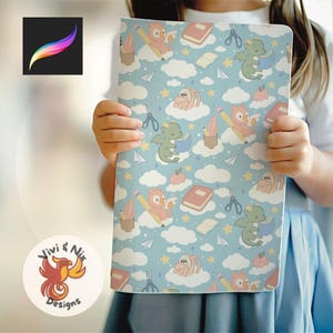 May include: A light blue notebook with a repeating pattern of cartoon dragons, owls, books, pencils, scissors, and clouds. The notebook is held by a person. The notebook has the logo "Vivi & Nix Designs" in a circle.