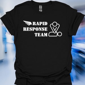 May include: Black t-shirt with the words "RAPID RESPONSE TEAM" in white, along with a wing graphic and a stylized image of a person performing CPR. The shirt is made of a soft material.