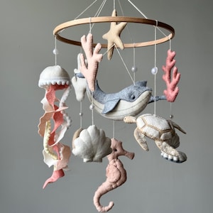 Puede incluir: Móvil para bebé hecho a mano con criaturas marinas de fieltro. Incluye una ballena, caballito de mar, medusa, estrella de mar, coral, concha y tortuga, suspendidos de un aro de madera con hilo y cuentas. Colores: azules, rosas y cremas suaves.