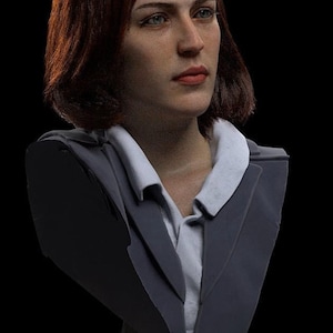 Op de afbeelding: Een bustebeeld van een vrouw met kort, donkerbruin haar. Ze draagt een donkergrijze blazer over een wit overhemd met kraag. De buste is gemonteerd op een zilveren standaard.